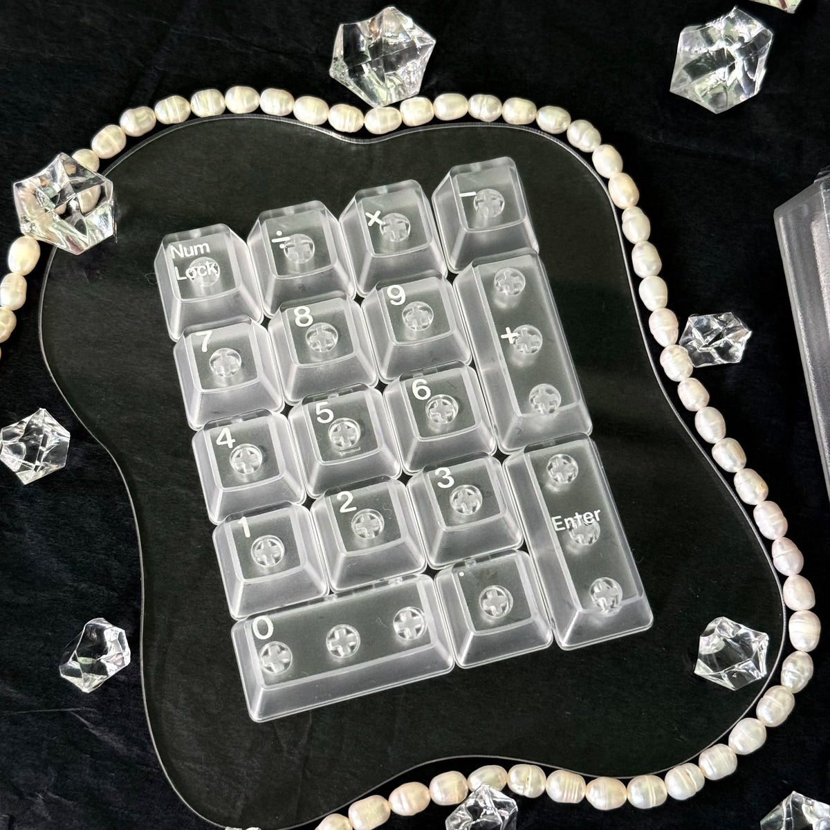 Translucent PC keycaps arranged on a black surface surrounded by pearl beads and crystal shards.