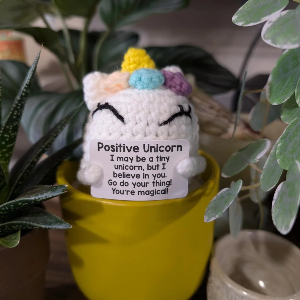 A handcrafted crochet unicorn doll with pastel colors sitting in a yellow pot.
