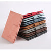 Une pile de porte-passeports en cuir de différentes couleurs, rouge, bleu, marron et gris.