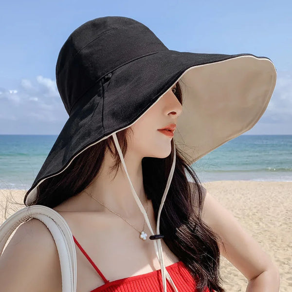 A woman wearing a black and beige reversible wide brim sun hat outdoors on a beach.