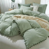 A light sage green duvet cover set with pom-pom trim and matching pillows on a bed.