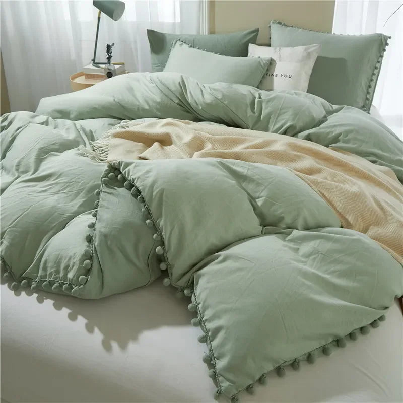 A light sage green duvet cover set with pom-pom trim and matching pillows on a bed.