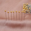 A collection of gold-colored precision quilting pins with silver shafts is displayed on a pink fabric.