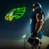 A muscular football player wearing a blue uniform holds an American football in front of a glowing neon green eagle sign.
