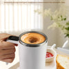 A white automatic coffee stirring cup is shown being held, with a small bowl of green tea leaves nearby.