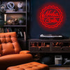 A neon sign featuring a bottle cap design for Nuka Cola displayed on a dark shelf next to a leather armchair.