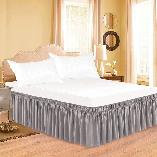 White bedding set featuring a ruffled bed skirt in gray and a matching elastic belt on a wooden bed frame.