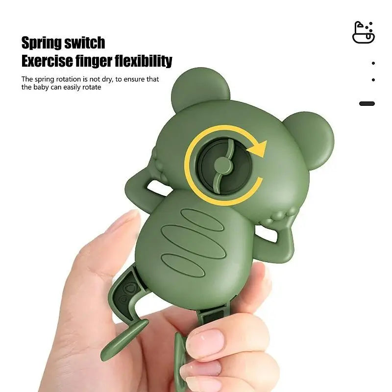 A hand holds a green silicone spring switch exercise finger flexibility toy shaped like a frog.
