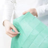 A hand is holding a green disposable toilet seat cover, showing the texture and fold of the product.