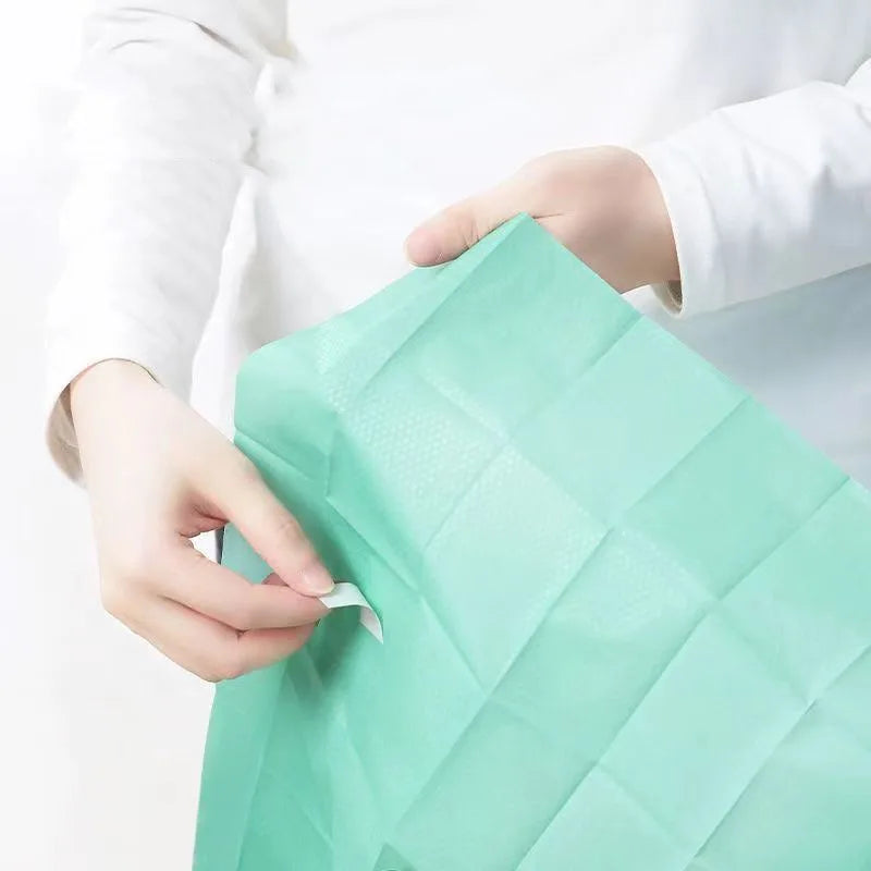 A hand is holding a green disposable toilet seat cover, showing the texture and fold of the product.