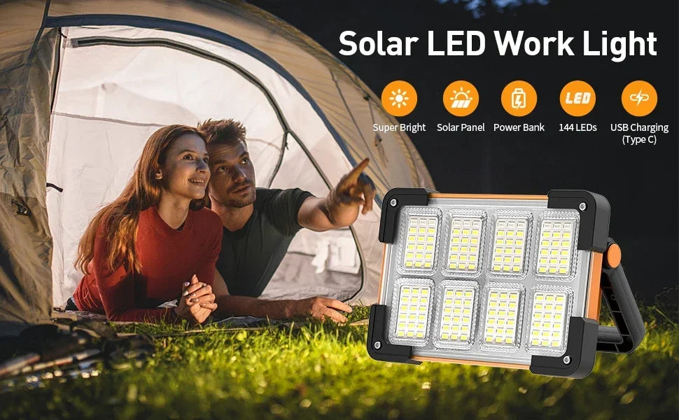 A portable solar LED work light is shown outdoors next to a tent, with two people in the background.