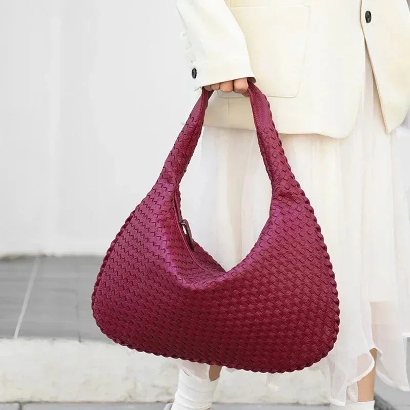 A woman holds a deep magenta woven leather hobo bag against a white background.