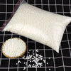 A white bag of natural soy wax granules next to loose white granules on a black grid surface.