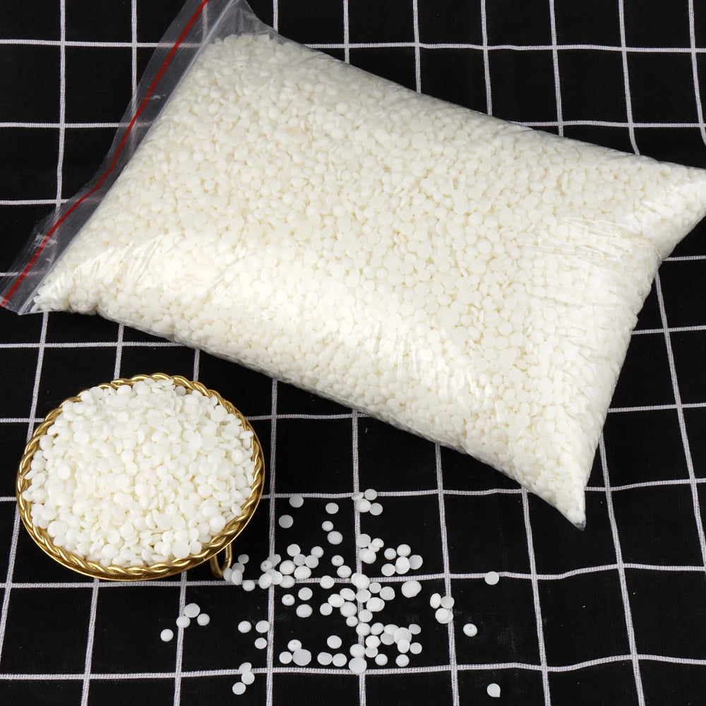 A white bag of natural soy wax granules next to loose white granules on a black grid surface.