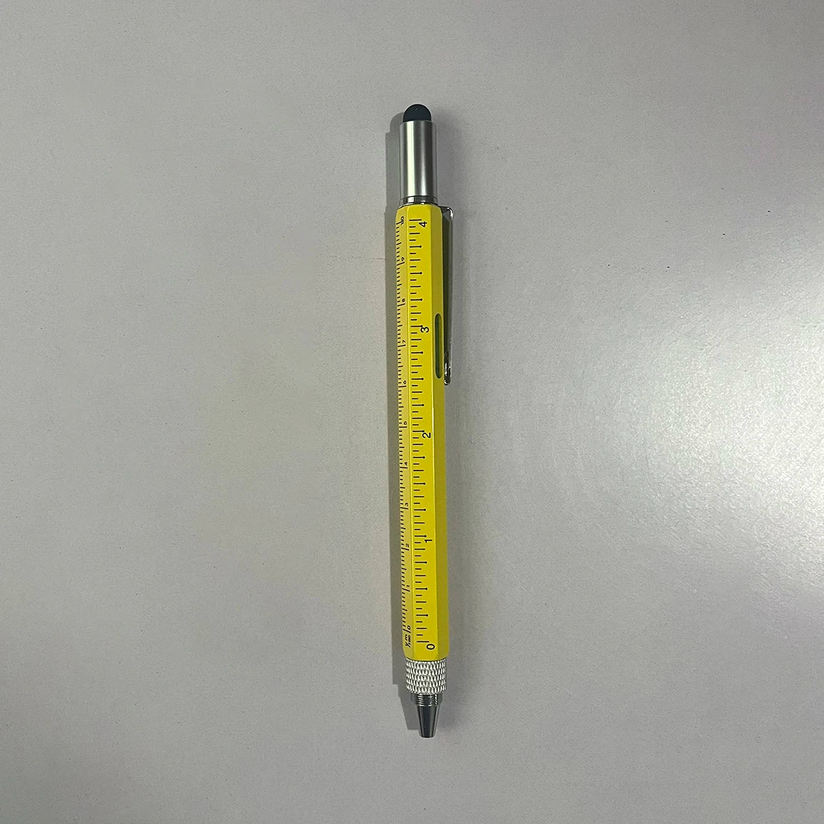 A silver and yellow 6-in-1 multitool pen with a clear scale is shown against a light gray background.