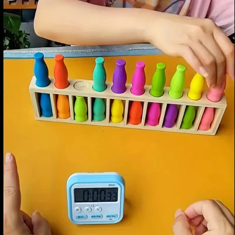 A hand is holding a wooden color matching puzzle set with 20 colored pieces arranged in a row on a yellow surface.