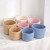 A collection of handwoven cotton rope storage baskets in various natural and pastel colors arranged on a white surface.