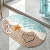 A beige and blue anti-slip bathroom rug featuring a sandy beach scene with starfish and a heart.
