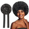 A woman models a black satin silk sleep bonnet tied in a bow, showing the fabric and design.