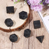 A set of matte black polyhedral dice resting on a wooden surface next to purple flowers.