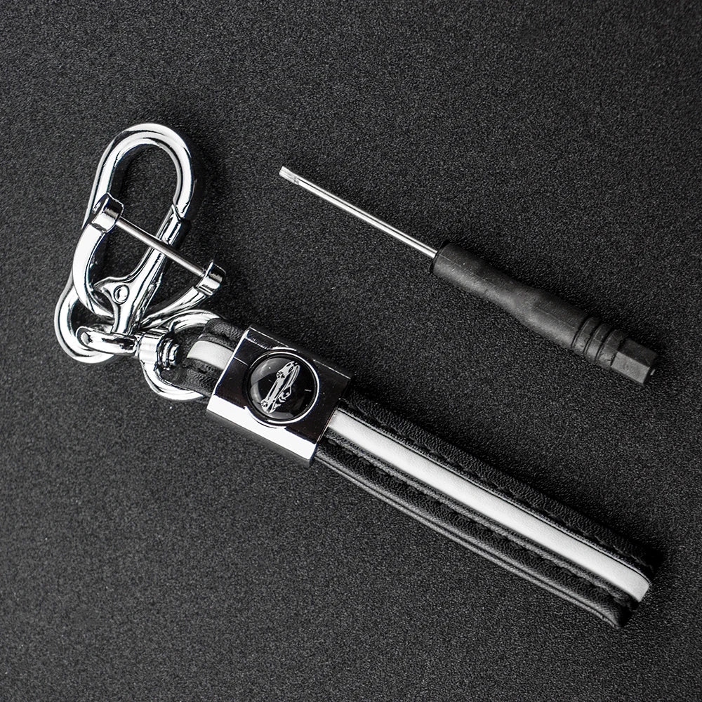A silver key fob with a protective black TPU cover and a metal tool is displayed on a dark surface.