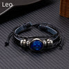 A black leather wrap bracelet featuring a blue gemstone charm on a dark gray textured background.