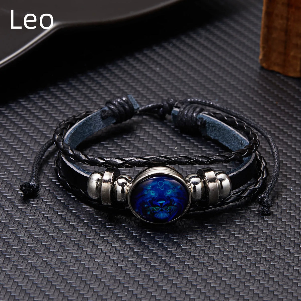 A black leather wrap bracelet featuring a blue gemstone charm on a dark gray textured background.