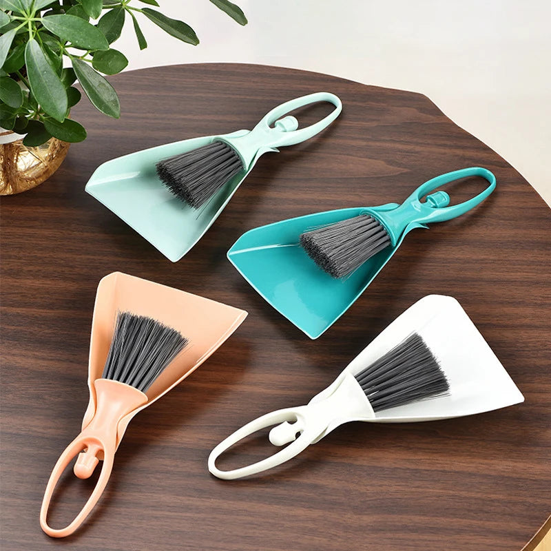 A set of three compact mini brooms and dustpans in teal, orange, and white resting on a dark wooden surface.