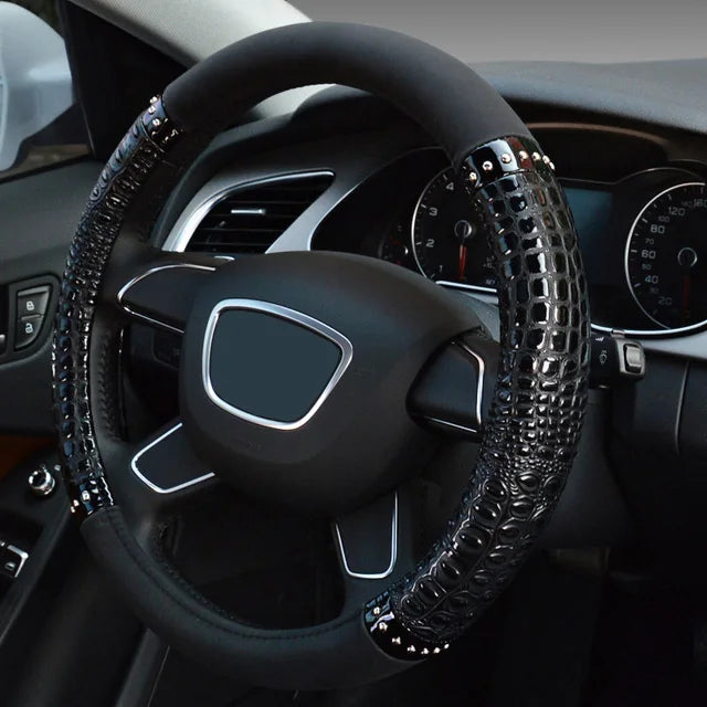 A close-up view of a black car steering wheel with crocodile grain leather covers and silver accents.