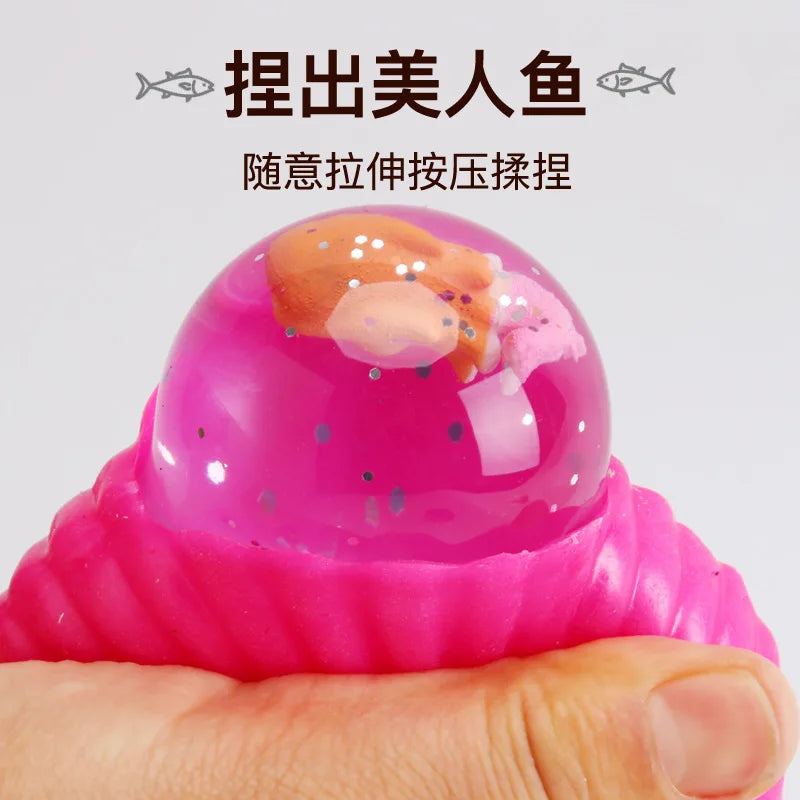 A close-up of a pink, translucent silicone fidget ball shaped like a mermaid shell is being squeezed by a hand.
