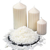 White natural soy wax flakes displayed next to two white pillar candles.