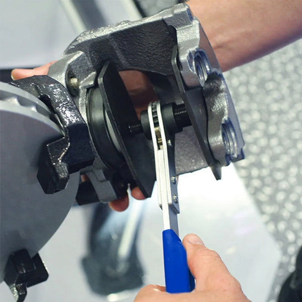 Une main utilise un outil pour rétracter manuellement le piston d'un étrier de frein.
