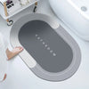 A gray bathroom mat with the word BATHROOM embossed on it is placed next to a white toilet bowl.