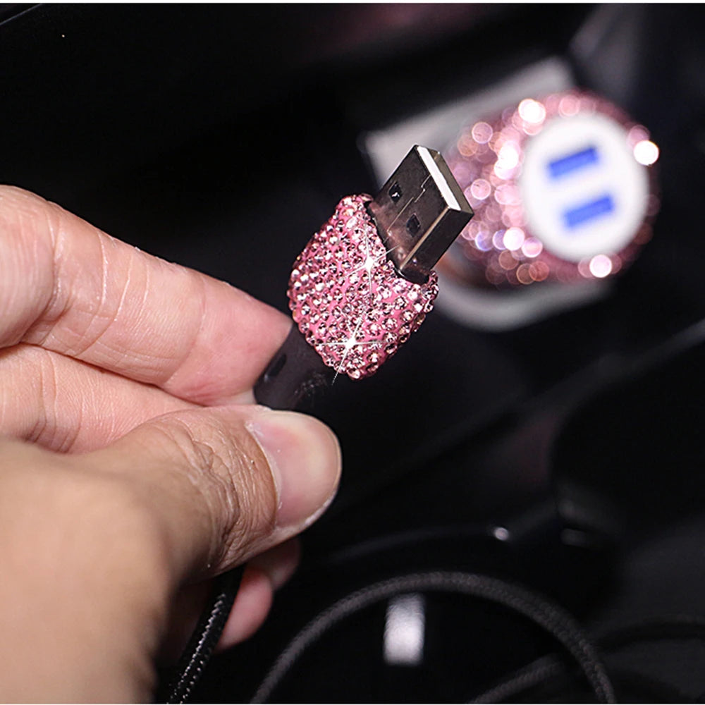 A hand holds a rhinestone dual USB car charger with fast charging feature, showing the pink and clear crystal design.