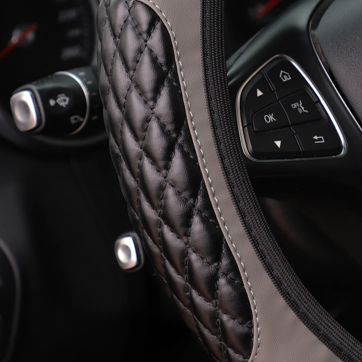Close-up of a black quilted steering wheel cover with stitching and a zipper, showing controls.