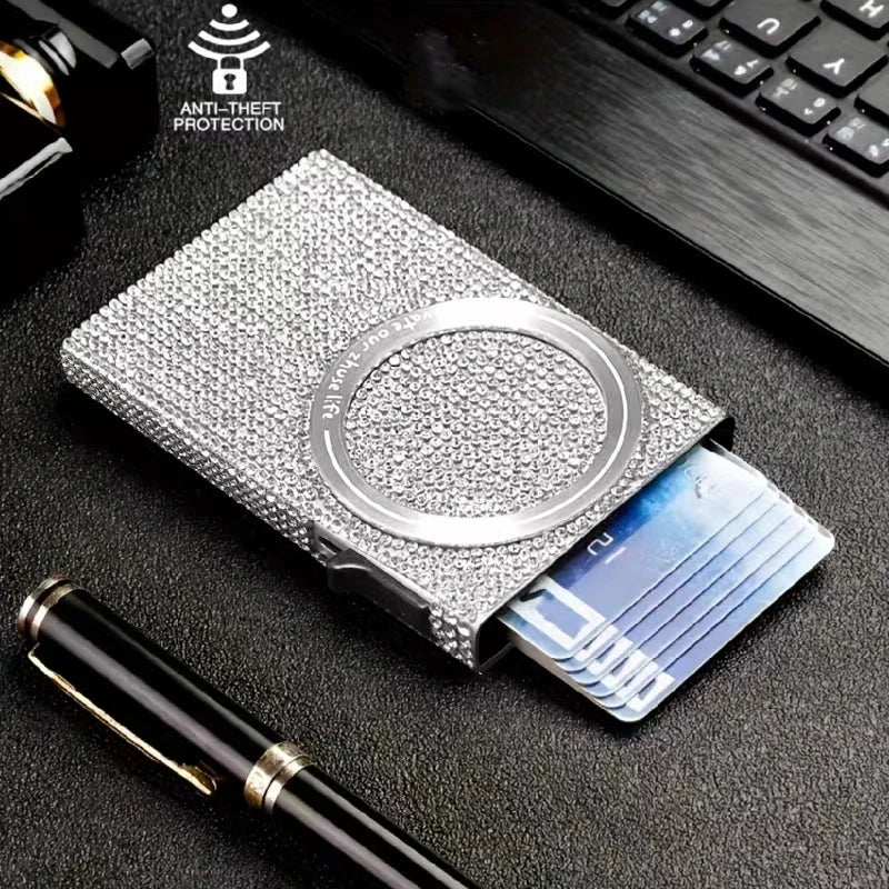 A slim aluminum RFID-blocking pop-up card wallet is shown next to a credit card and a pen on a dark surface.