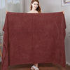 A woman holds up a large, deep red microfiber bath towel for display.