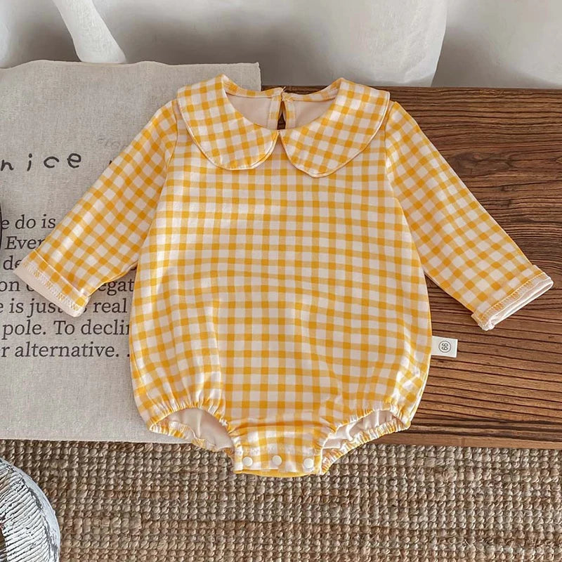 A yellow and white gingham long-sleeved romper for a baby girl lying on a wooden surface.