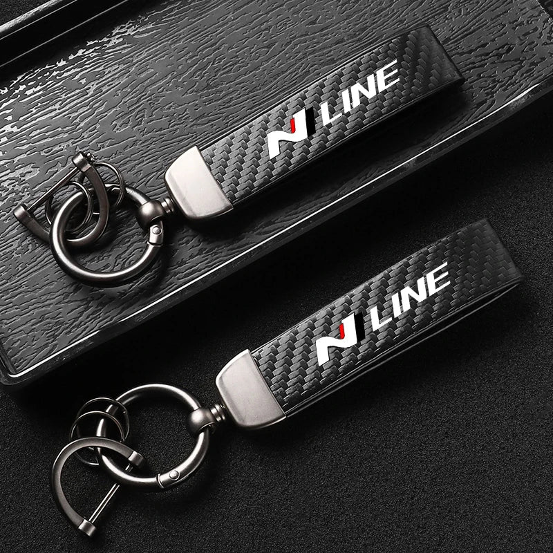 A close-up shot of a black carbon fiber style leather keychain with a silver swivel buckle.