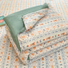 A stack of light patterned quilts in pale orange and blue tones lying on a striped fabric background.