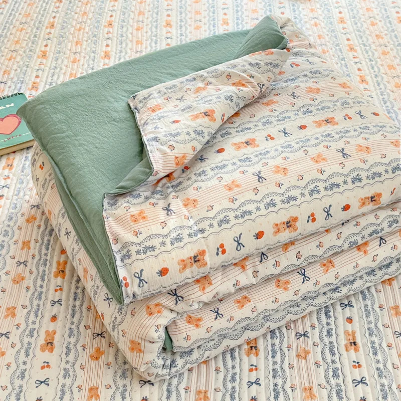 A stack of light patterned quilts in pale orange and blue tones lying on a striped fabric background.