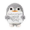 A gray crocheted penguin plush toy holding a white sign with the text Positive penguin I may be a tiny penguin but I believe 