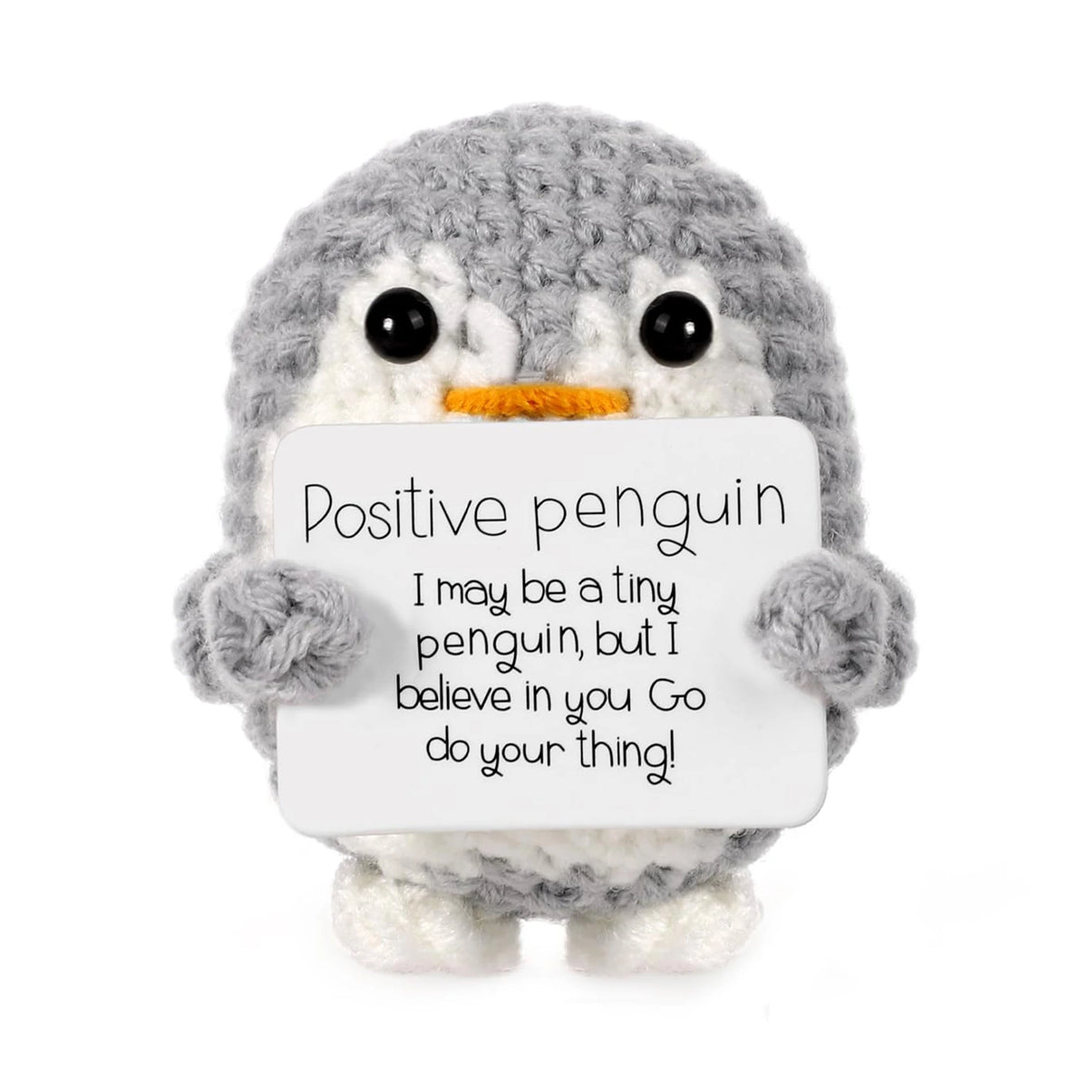A gray crocheted penguin plush toy holding a white sign with the text Positive penguin I may be a tiny penguin but I believe 