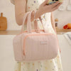 A light pink quilted insulated lunch tote bag with a zipper is being held by a person.