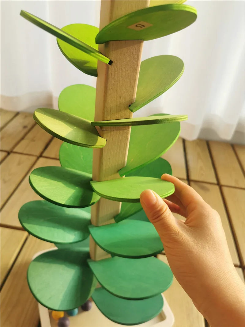 Holzbaumstruktur mit grünen Blütenblättern und einer Marmorbahn, gehalten von einer Hand.