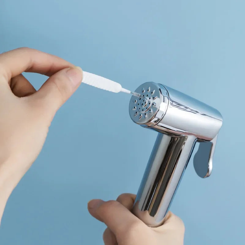 A hand is holding a shower cleaning brush set with an anti-clogging nozzle cleaner against a light blue background.
