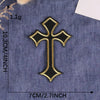 A black and gold embroidered cross patch on a denim fabric background.