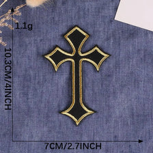 A black and gold embroidered cross patch on a denim fabric background.
