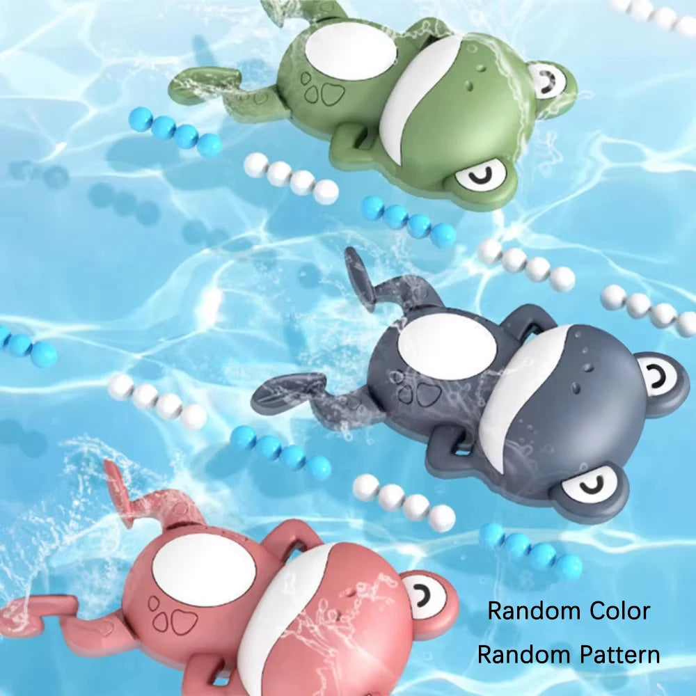 A collection of three wind-up swimming frog bath toys in green, gray, and pink floating in clear water.