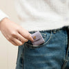 A hand places a small lavender PU leather jewelry organizer pouch into the pocket of blue denim jeans.